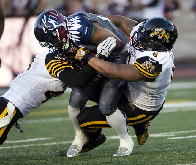 Montreal Alouettes running back Tyrell Sutton (20) is tackled by Hamilton Tiger-Cats defensive back Erik Harris, left, and Hamilton Tiger-Cats defensive tackle Bryan Hall (6) during second quarter CFL action Thursday, July 16, 2015 in Montreal.THE CANADIAN PRESS/Ryan Remiorz